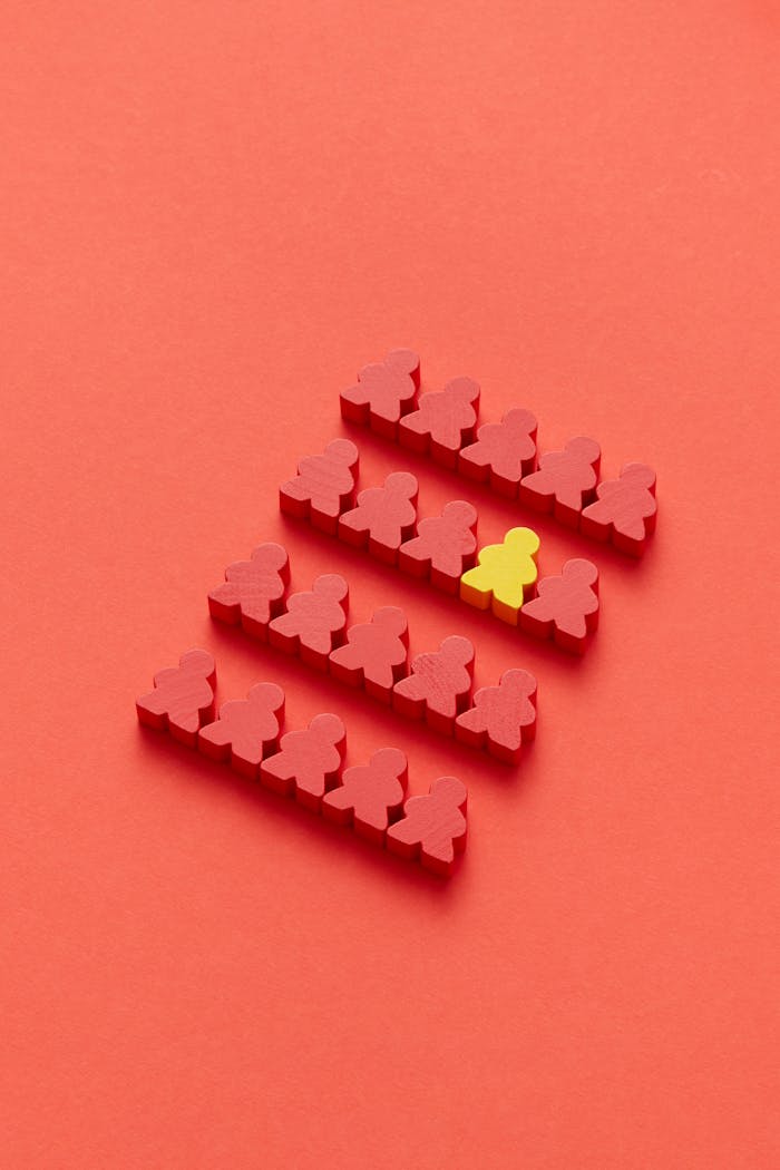 A group of red meeples with one yellow meeple standing out on a red background, symbolizing individuality.