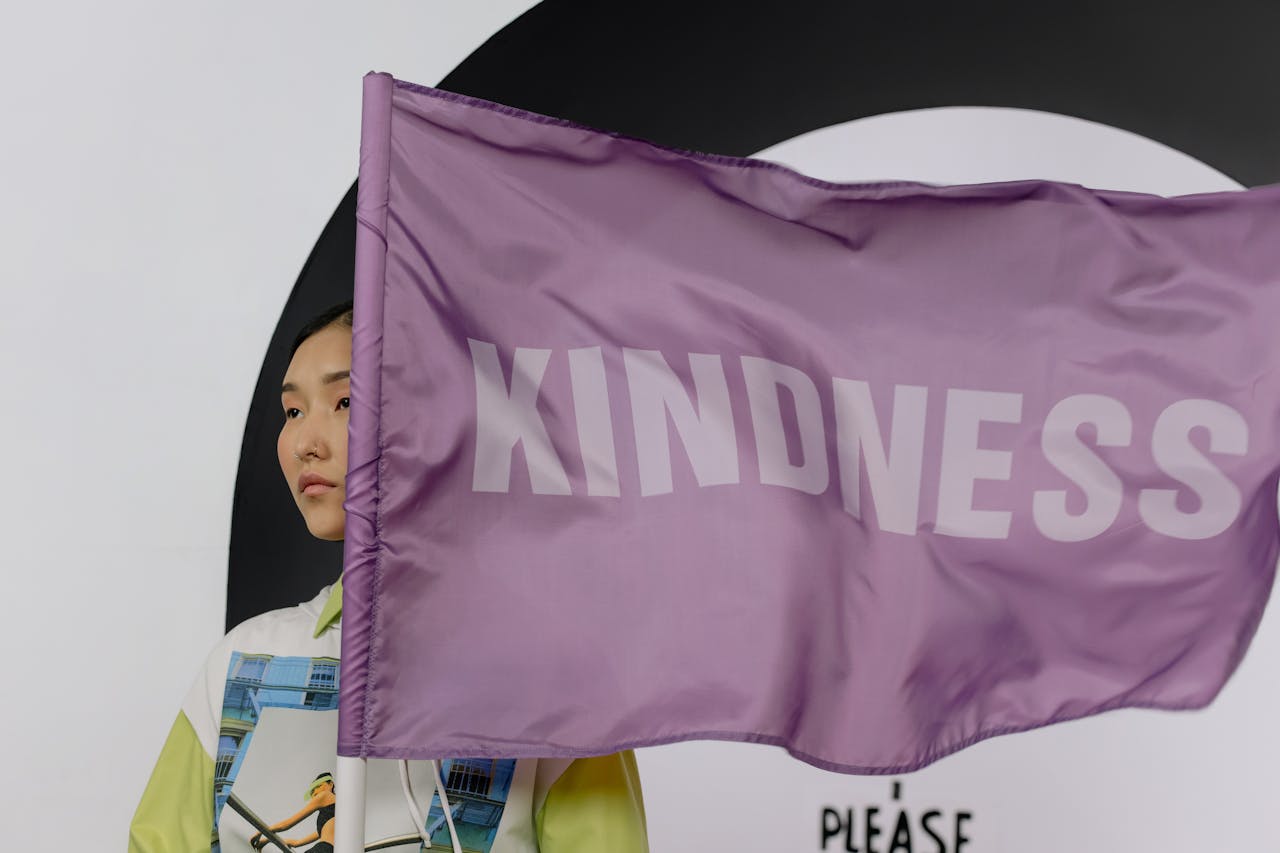 Asian woman holding a colorful Kindness flag against a modern background.